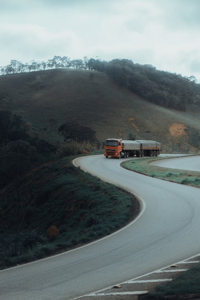 A red truck drives on a winding road in a mountainous landscape, showcasing scenic transportation.